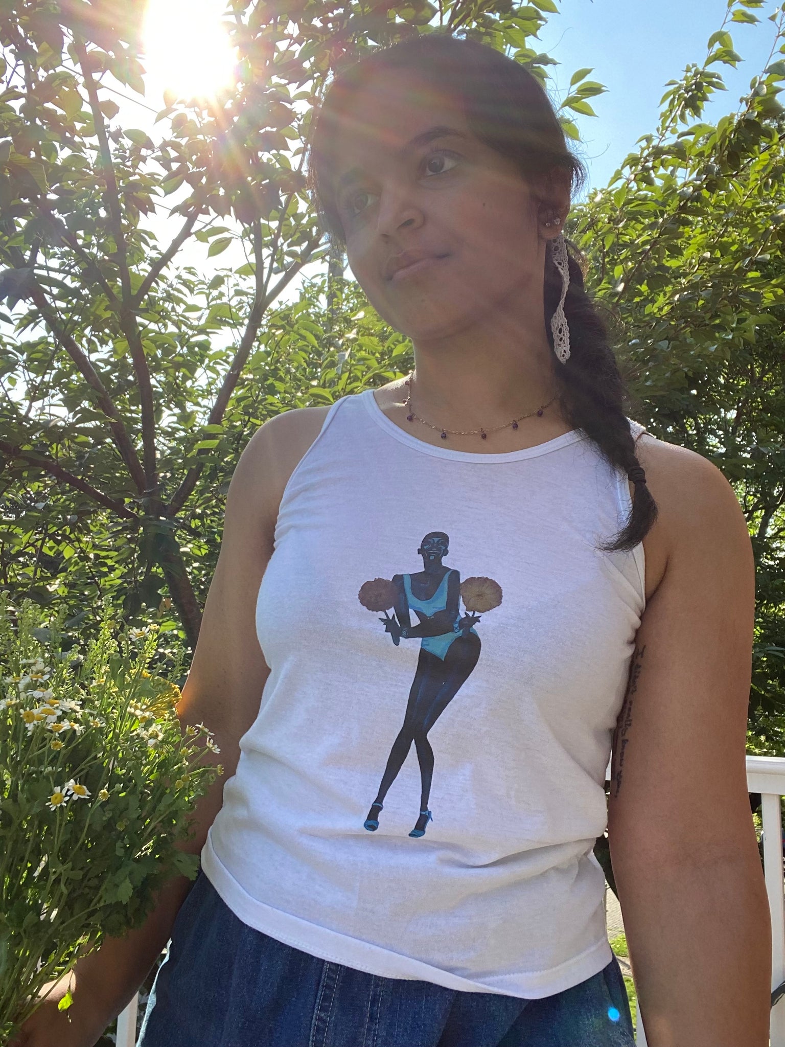 A girl holding flowers and posing in a white upcycled tank top with an image on it of supermodel Adut Akech