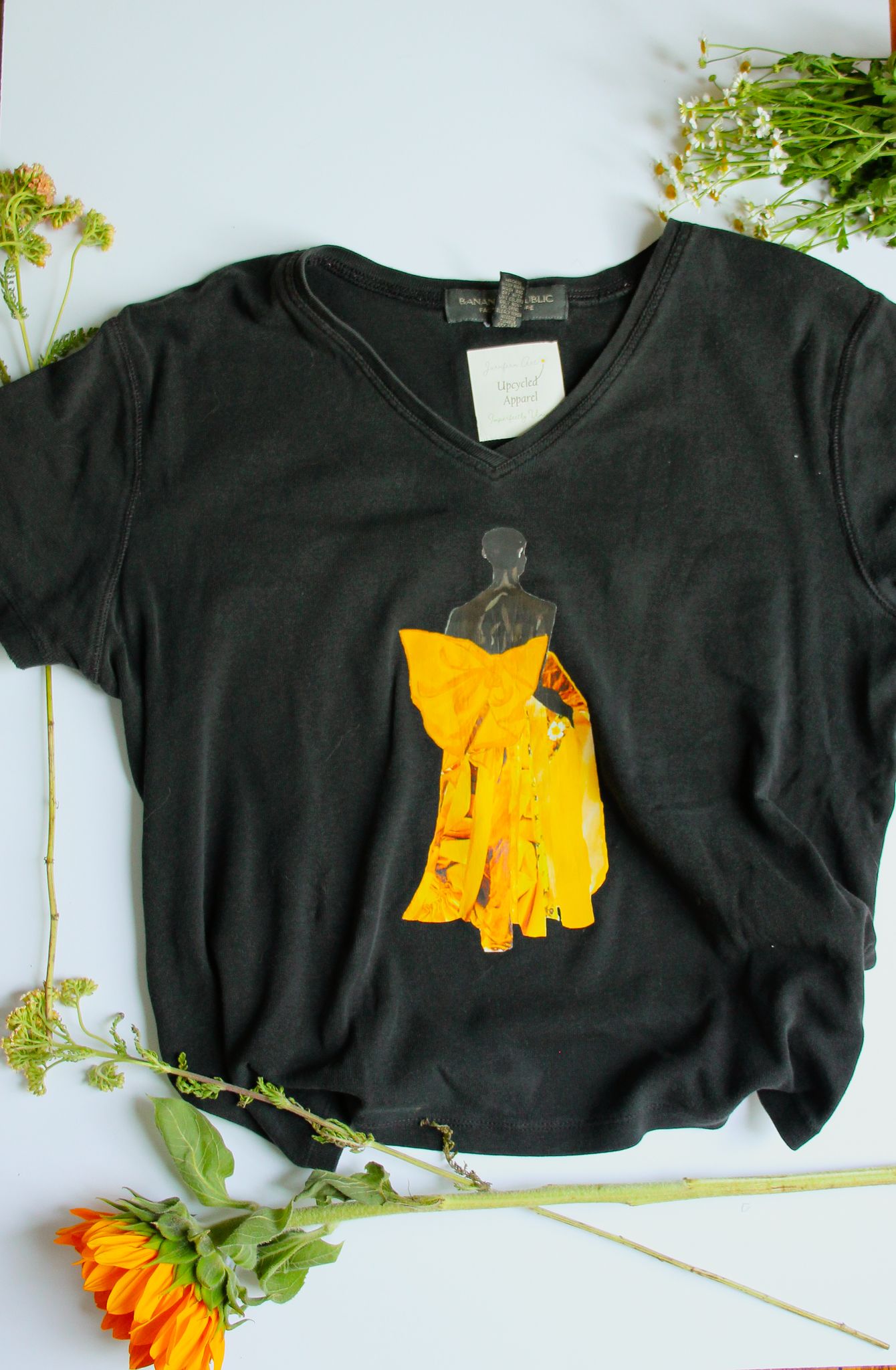 An upcycled black V-neck t-shirt with an image of model Akiima Ajak wearing a yellow gown on it