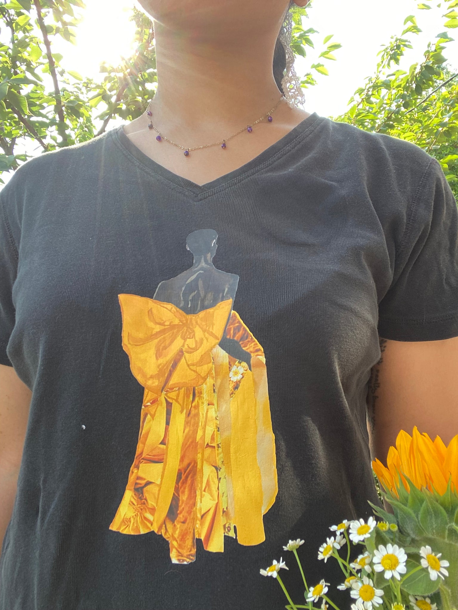 A girl modeling an upcycled black V-neck t-shirt with an image on it of model Akiima Ajak wearing a yellow gown