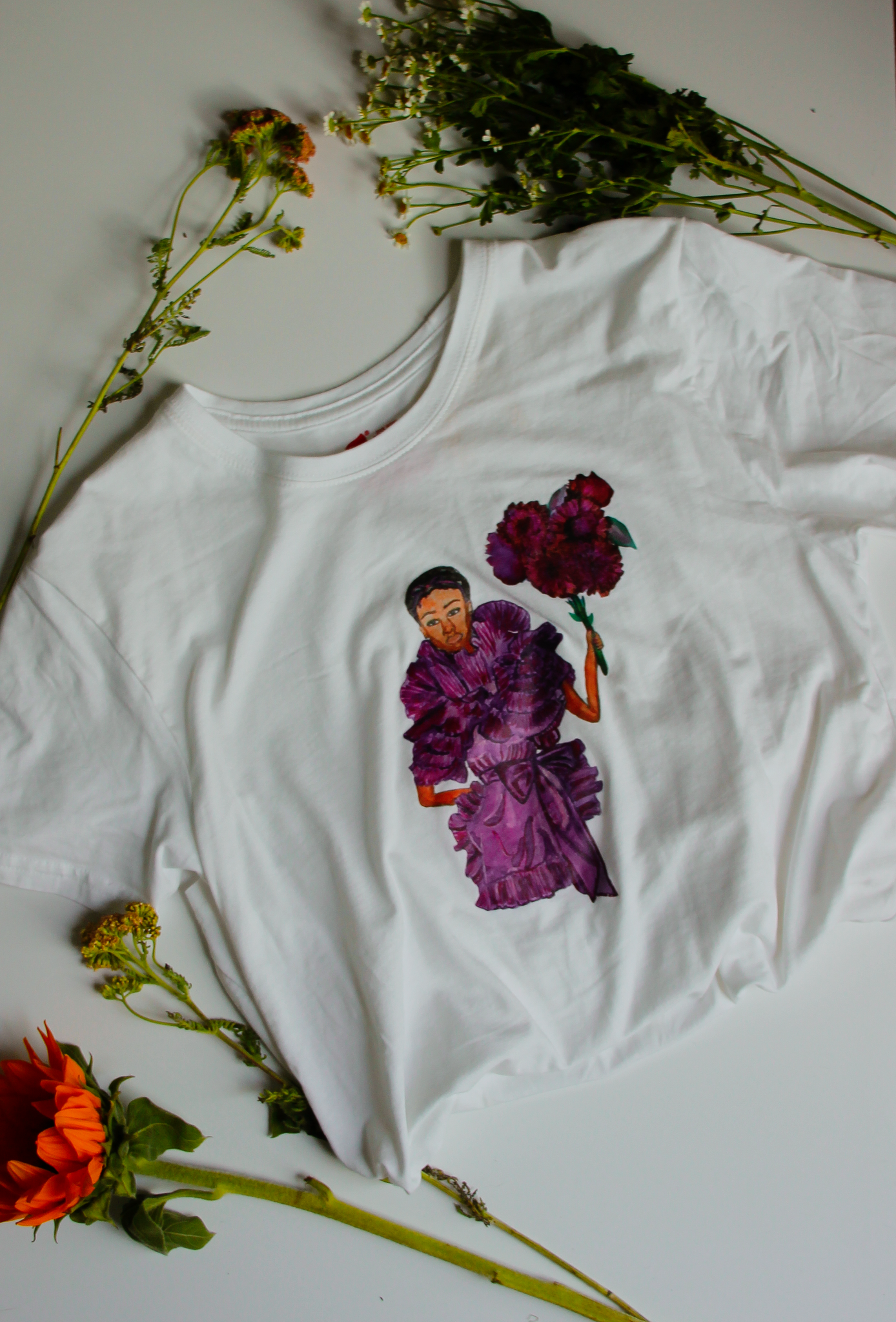 An upcycled white t-shirt with an illustration on it of model Janaye Furman wearing a ruffled purple gown