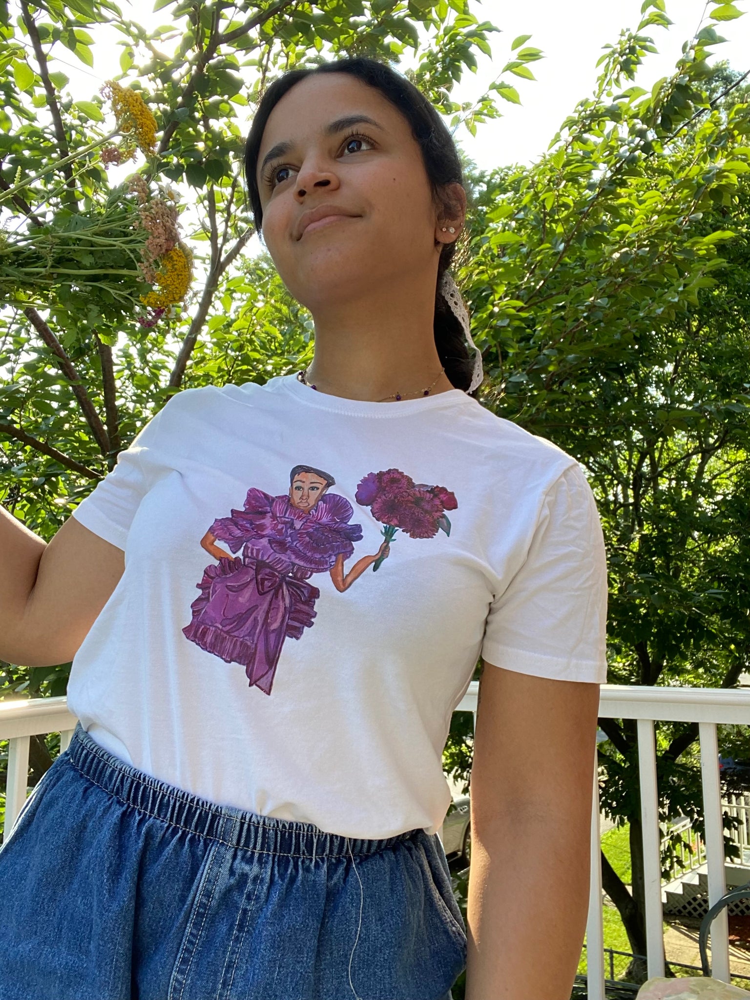 A girl holding flowers and modeling an upcycled white t-shirt with an image on it of model Janaye Furman wearing a purple ruffled gown
