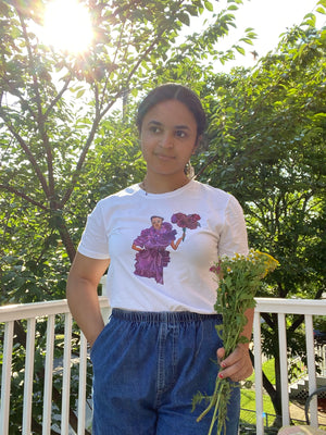 A girl holding flowers and wearing denim shorts and an upcycled white t-shirt with an illustration on it of model Janaye Furman in a purple ruffled gown