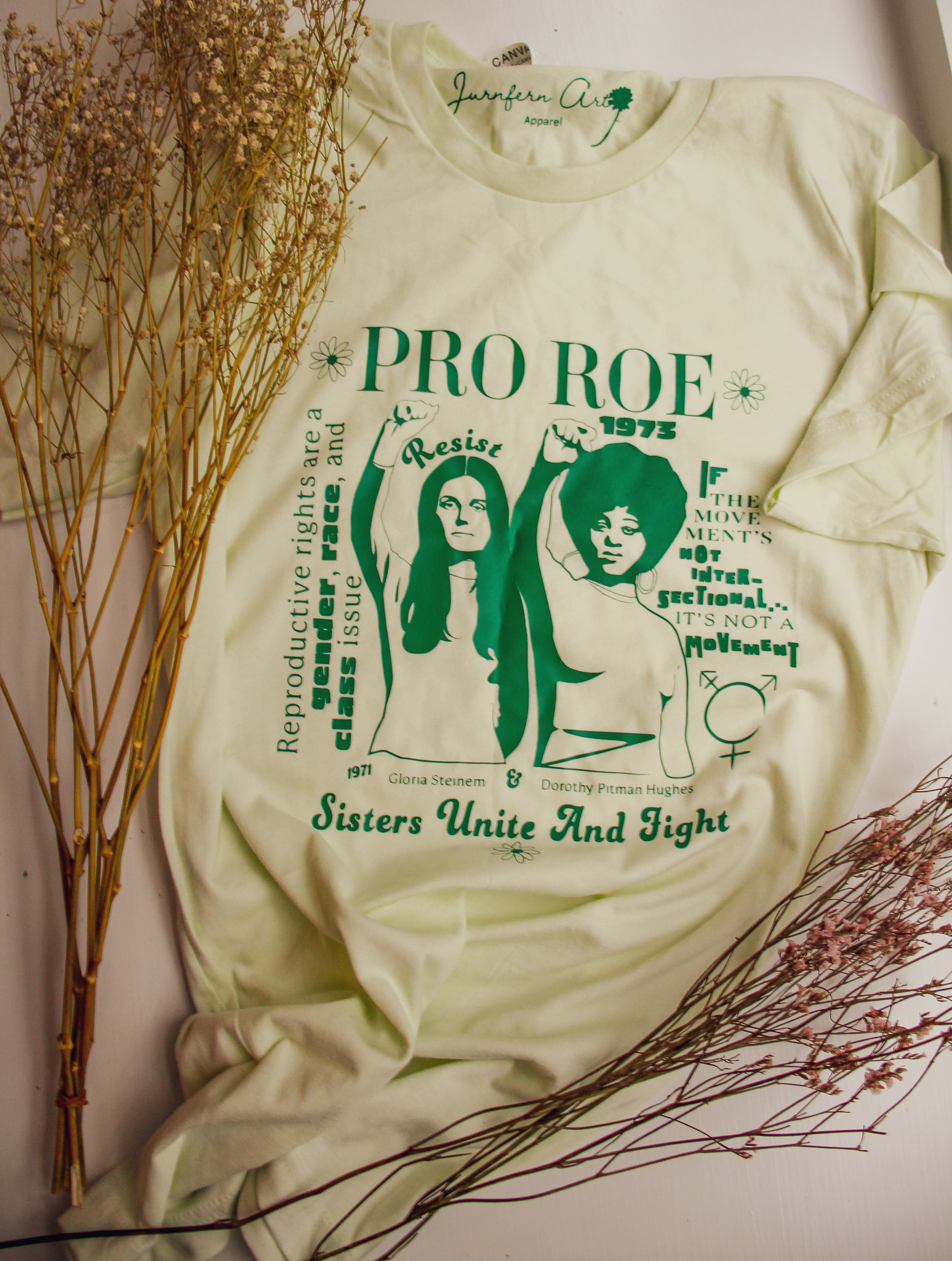 A t-shirt with an image on it of Gloria Steinem and Dorothy Pitman and text that reads 'PRO ROE,' surrounded by dry flowers