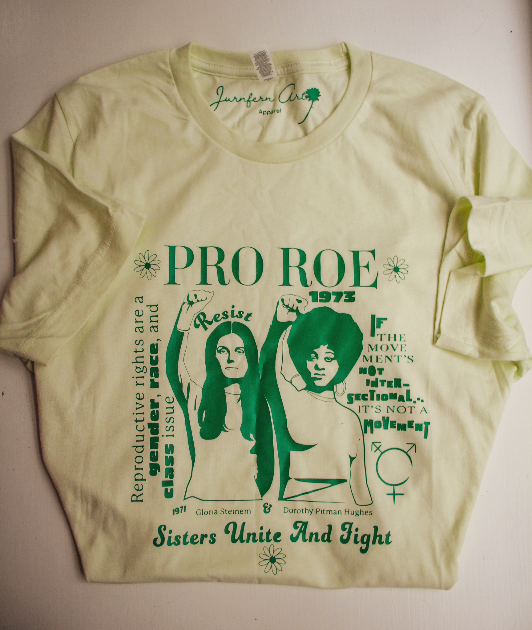 A t-shirt with a green printed image on it of Gloria Steinem and Dorothy Pitman, with text that reads 'PRO ROE' and 'Sisters Unite and Fight'