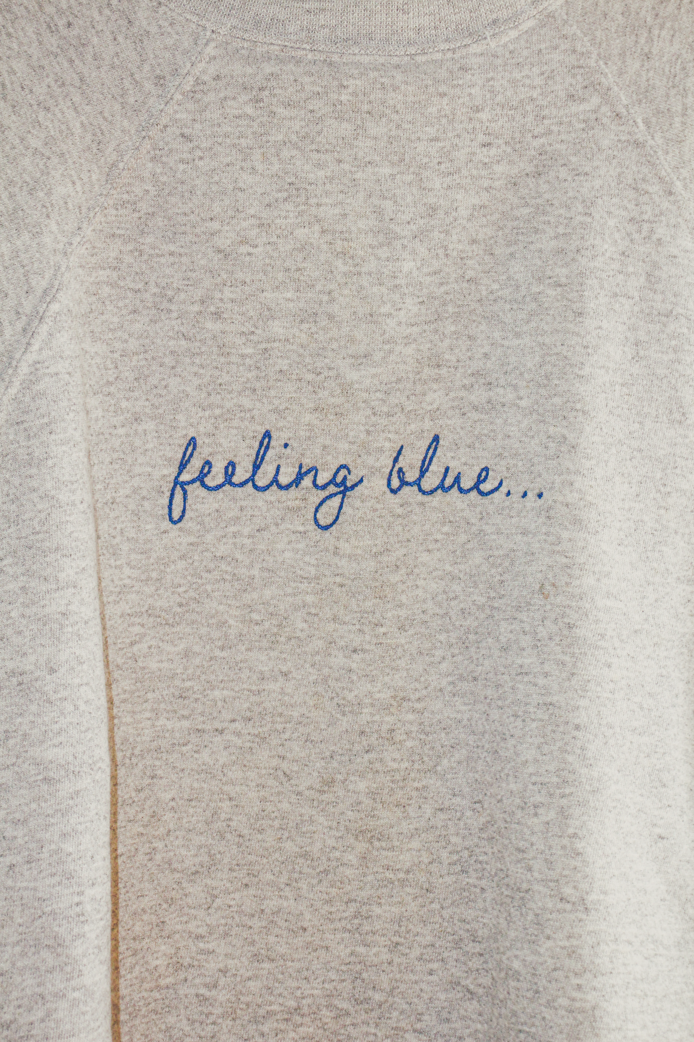 A gray sweatshirt with blue embroidered text on it that reads "feeling blue..."