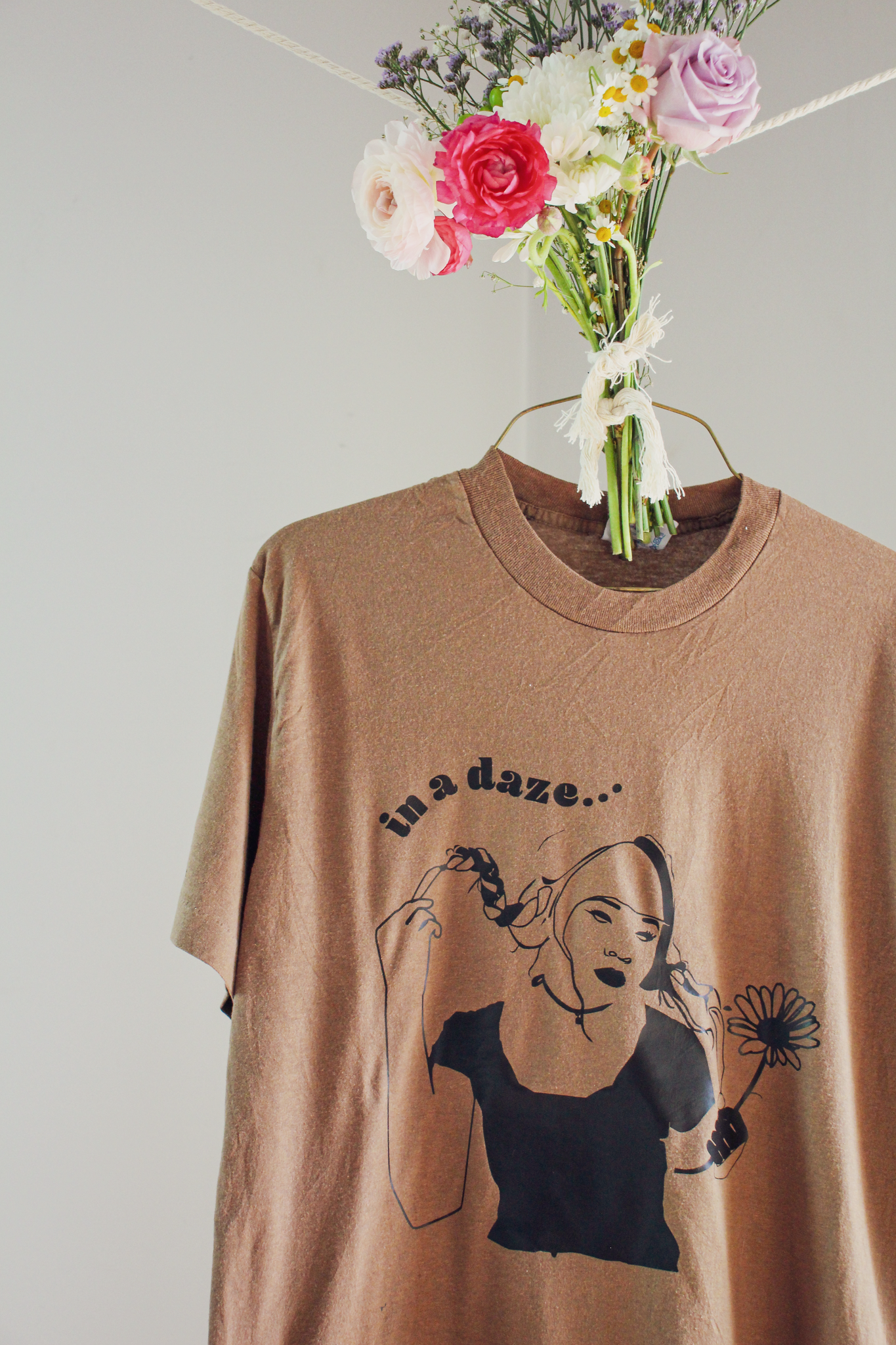 A brown t-shirt with a black illustration of a girl holding a flower and text that reads "in a daze...."