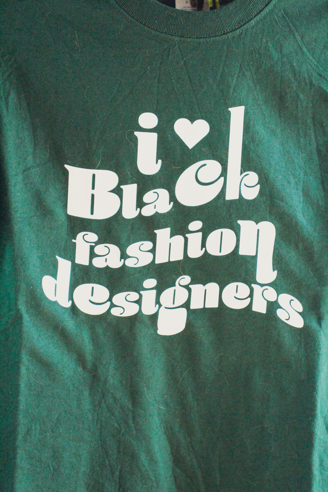 A dark green t-shirt with retro style text on it that reads "i love Black fashion designers"