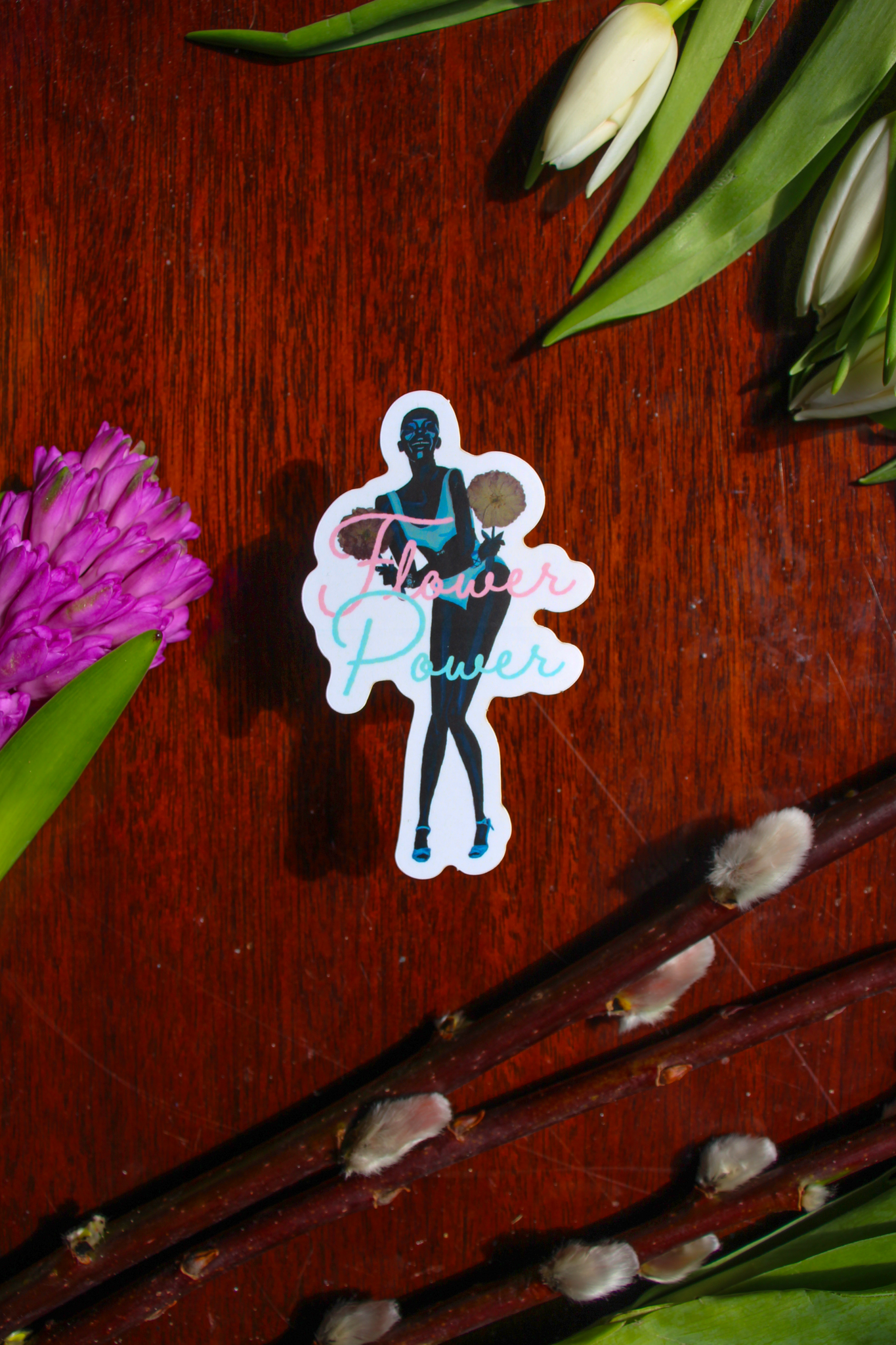 A sticker of an image of model Adut Akech wearing a Chanel one-piece and holding oversized pressed flowers, with the words "Flower Power" in front