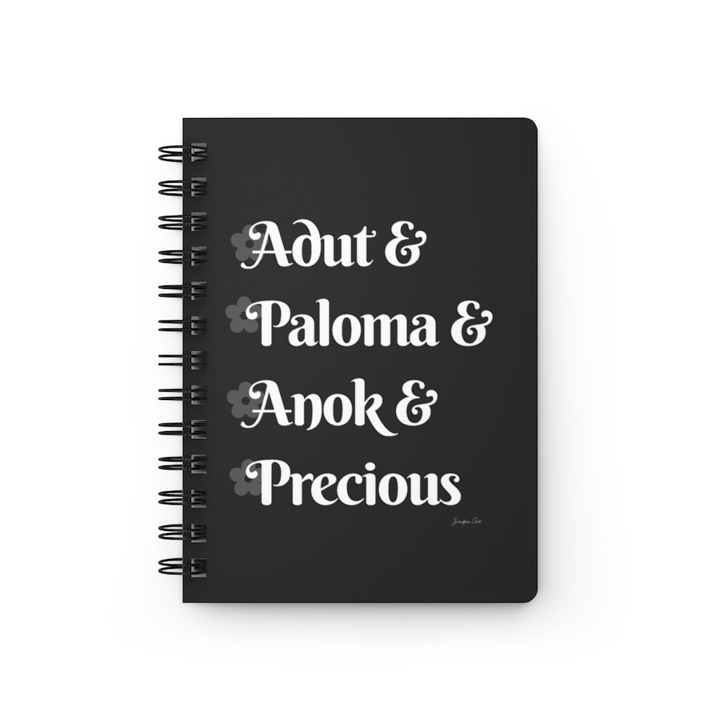 A black notebook with white text that reads "Adut & Paloma & Anok & Precious" in reference to the Black models Adut Akech, Paloma Elsesser, Anok Yai, and Precious Lee