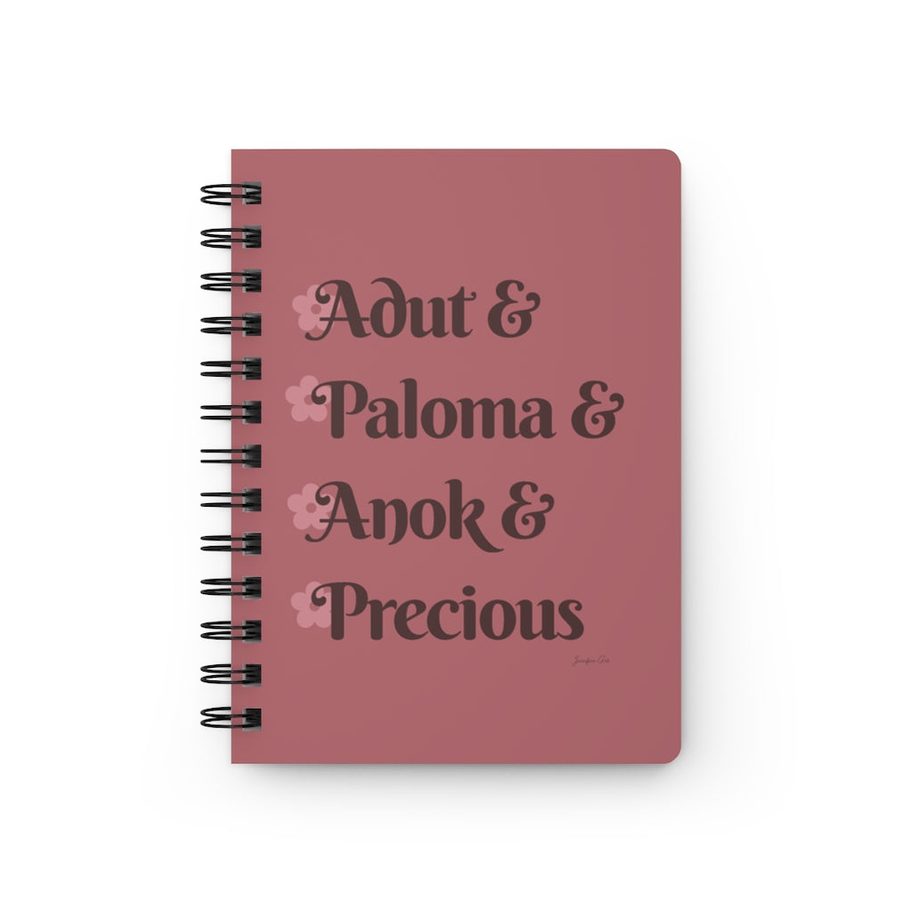 A pink notebook with dark pink text that reads "Adut & Paloma & Anok & Precious" in reference to the Black models Adut Akech, Paloma Elsesser, Anok Yai, and Precious Lee