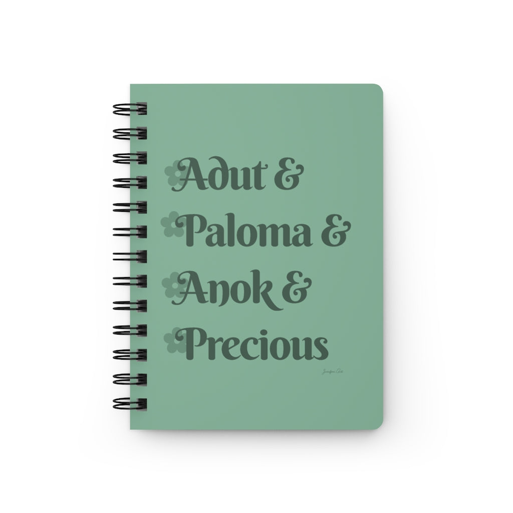 A light green notebook with dark green text that reads "Adut & Paloma & Anok & Precious" in reference to the Black models Adut Akech, Paloma Elsesser, Anok Yai, and Precious Lee