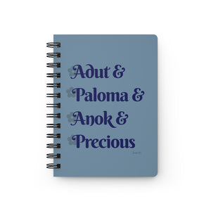 A light blue notebook with dark blue text that reads "Adut & Paloma & Anok & Precious" in reference to the Black models Adut Akech, Paloma Elsesser, Anok Yai, and Precious Lee