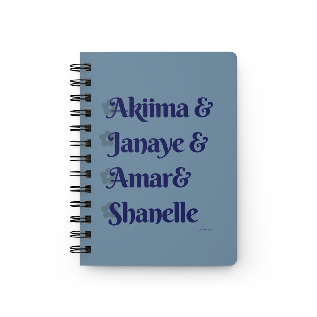 A light blue notebook with dark blue text that reads "Akiima & Janaye & Amar & Shanelle" in reference to the Black models Akiima Ajak, Janaye Furman, Amar Akway, and Shanelle Nyasiase