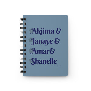 A light blue notebook with dark blue text that reads "Akiima & Janaye & Amar & Shanelle" in reference to the Black models Akiima Ajak, Janaye Furman, Amar Akway, and Shanelle Nyasiase