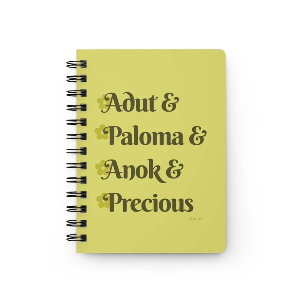 A yellow notebook with dark yellow text that reads "Adut & Paloma & Anok & Precious" in reference to the Black models Adut Akech, Paloma Elsesser, Anok Yai, and Precious Lee