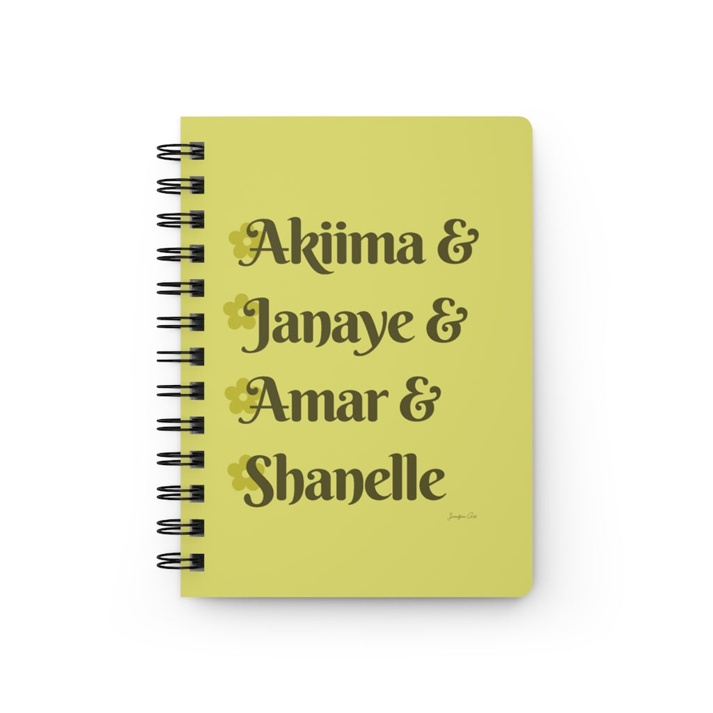 A yellow notebook with dark yellow text that reads "Akiima & Janaye & Amar & Shanelle" in reference to the Black models Akiima Ajak, Janaye Furman, Amar Akway, and Shanelle Nyasiase