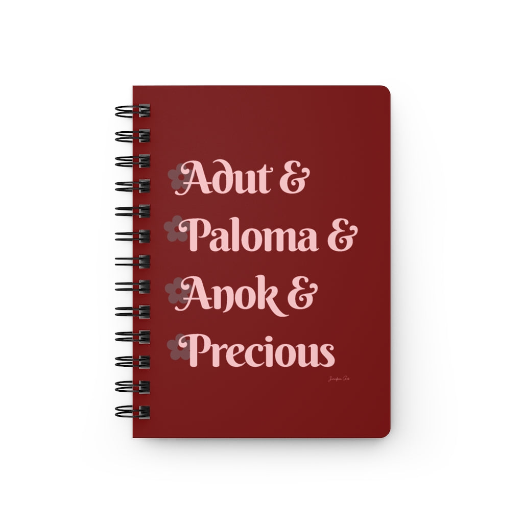 A red notebook with light pink text that reads "Adut & Paloma & Anok & Precious" in reference to the Black models Adut Akech, Paloma Elsesser, Anok Yai, and Precious Lee