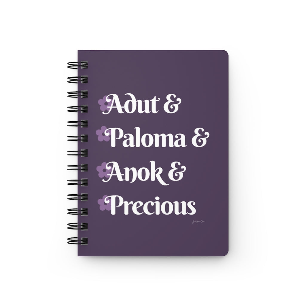 A lavender notebook with white text that reads "Adut & Paloma & Anok & Precious" in reference to the Black models Adut Akech, Paloma Elsesser, Anok Yai, and Precious Lee