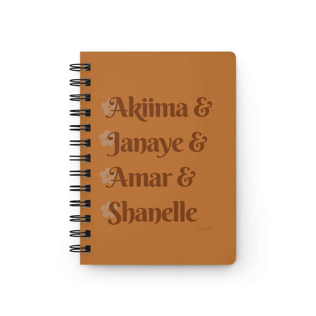 An orange notebook with dark orange text that reads "Akiima & Janaye & Amar & Shanelle" in reference to the Black models Akiima Ajak, Janaye Furman, Amar Akway, and Shanelle Nyasiase