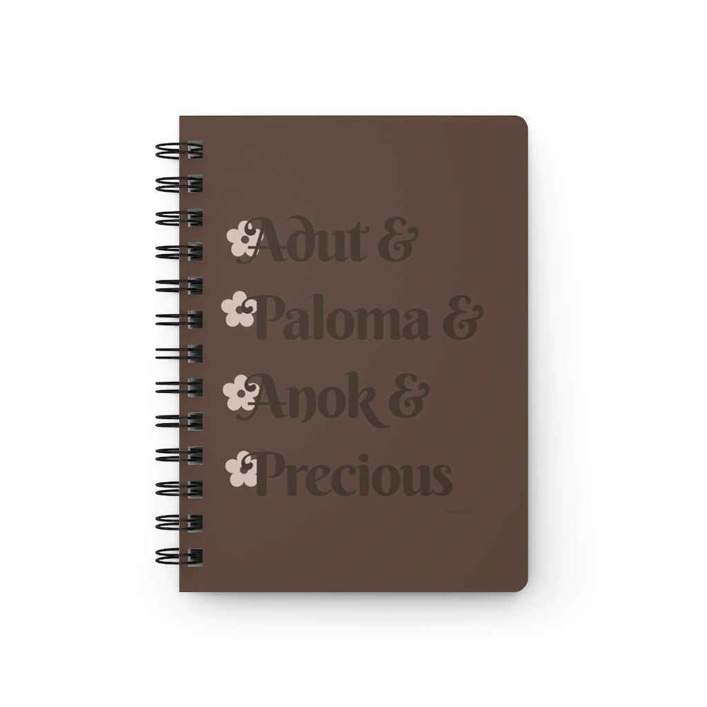 A brown notebook with dark brown text that reads "Adut & Paloma & Anok & Precious" in reference to the Black models Adut Akech, Paloma Elsesser, Anok Yai, and Precious Lee