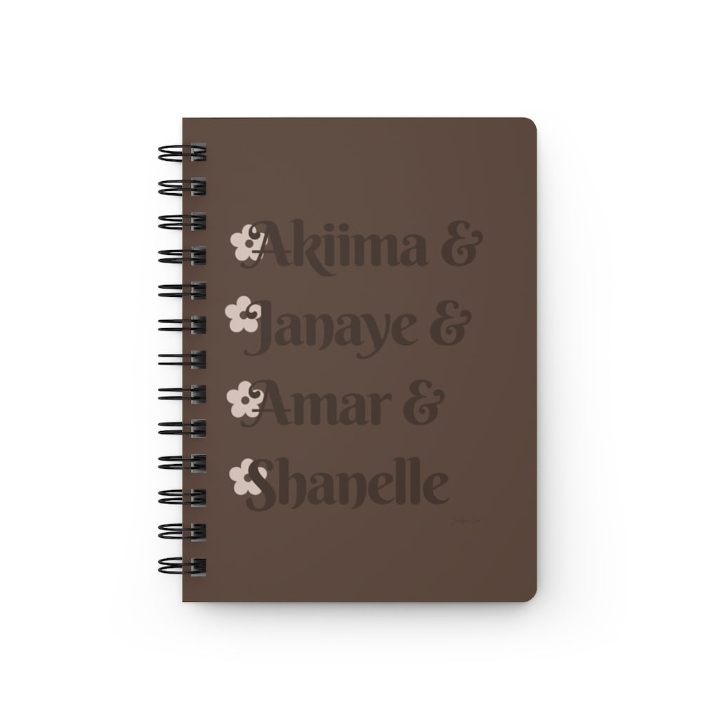 A brown notebook with dark brown text that reads "Akiima & Janaye & Amar & Shanelle" in reference to the Black models Akiima Ajak, Janaye Furman, Amar Akway, and Shanelle Nyasiase