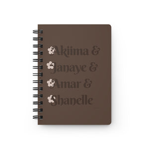 A brown notebook with dark brown text that reads "Akiima & Janaye & Amar & Shanelle" in reference to the Black models Akiima Ajak, Janaye Furman, Amar Akway, and Shanelle Nyasiase