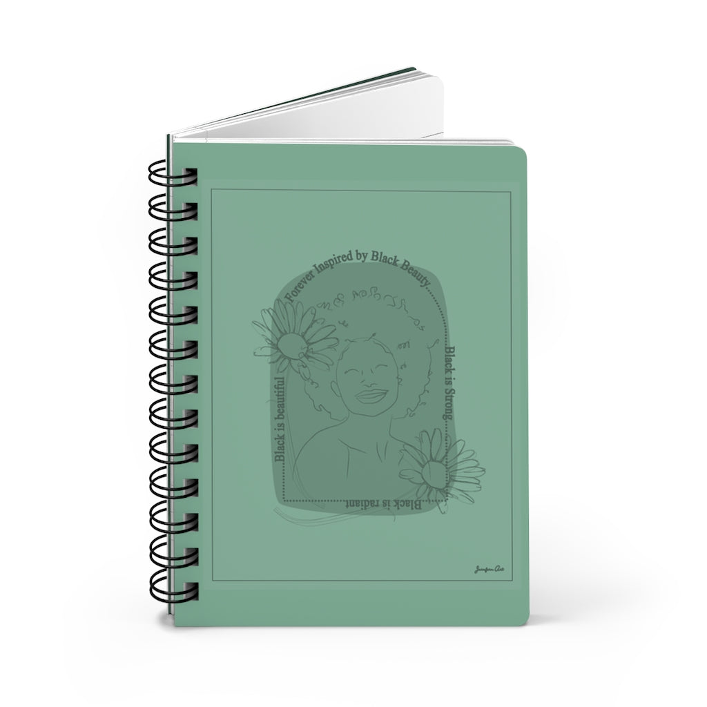 A monochrome green spiral journal with a line drawing on the cover of a Black woman with an afro surrounded by flowers and text that reads "Forever Inspired by Black Beauty"