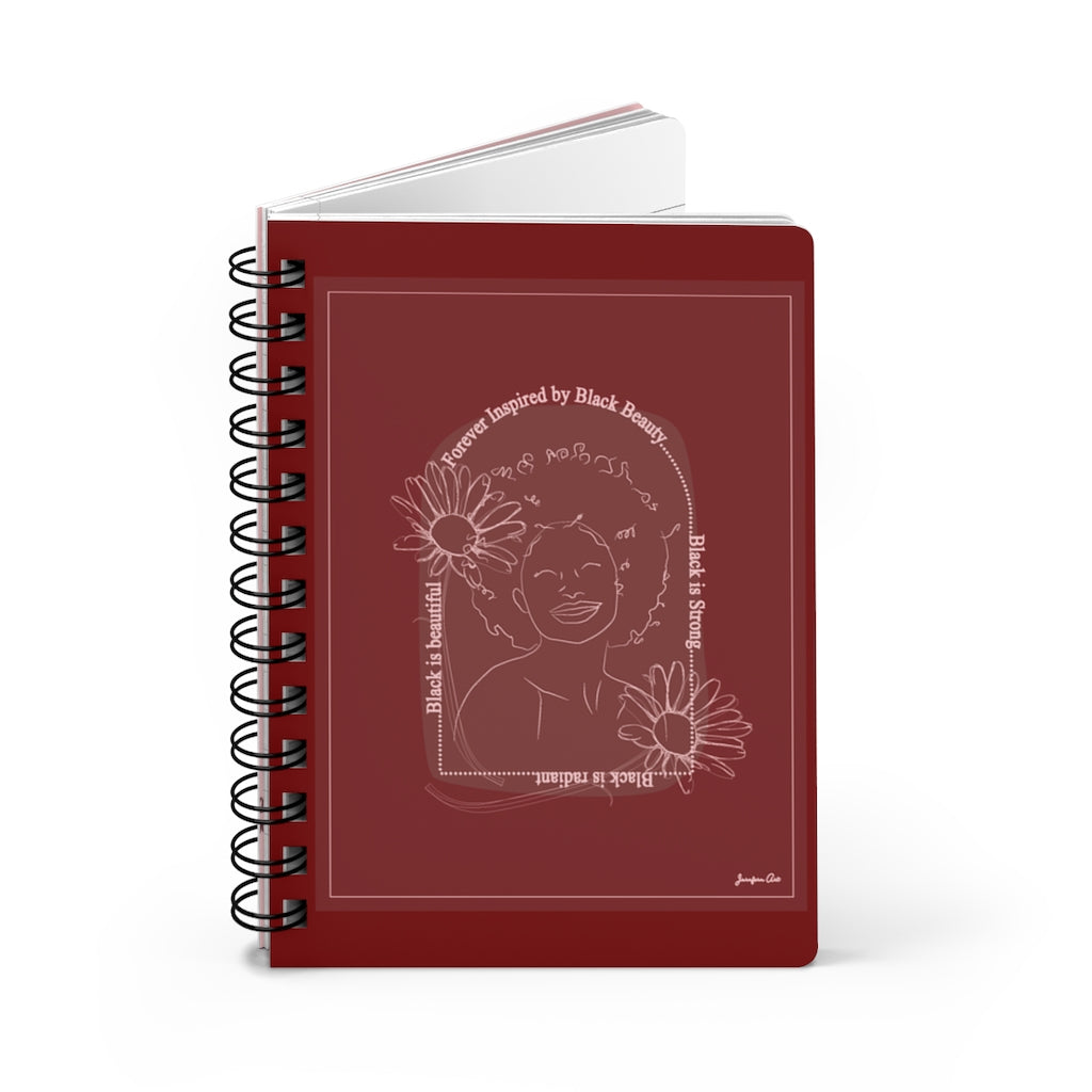 A monochrome red spiral journal with a line drawing on the cover of a Black woman with an afro surrounded by flowers and text that reads "Forever Inspired by Black Beauty"