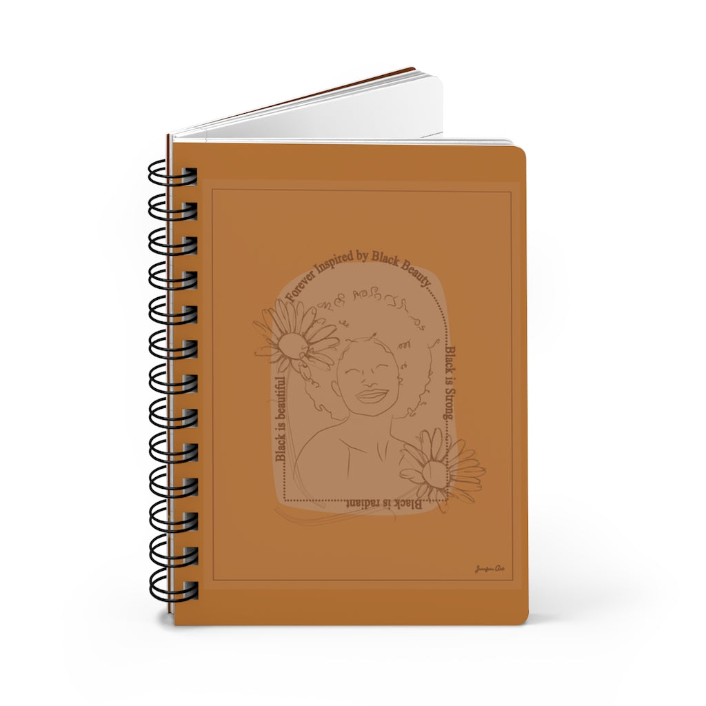 A monochrome orange spiral journal with a line drawing on the cover of a Black woman with an afro surrounded by flowers and text that reads "Forever Inspired by Black Beauty"