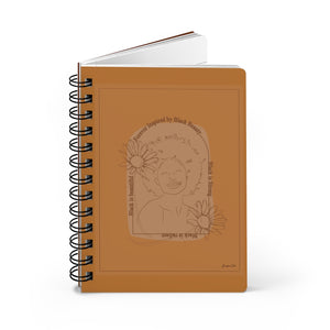 A monochrome orange spiral journal with a line drawing on the cover of a Black woman with an afro surrounded by flowers and text that reads "Forever Inspired by Black Beauty"