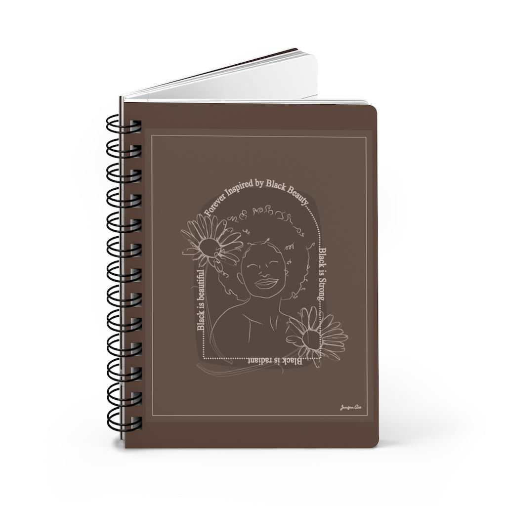 A monochrome brown spiral journal with a line drawing on the cover of a Black woman with an afro surrounded by flowers and text that reads "Forever Inspired by Black Beauty"