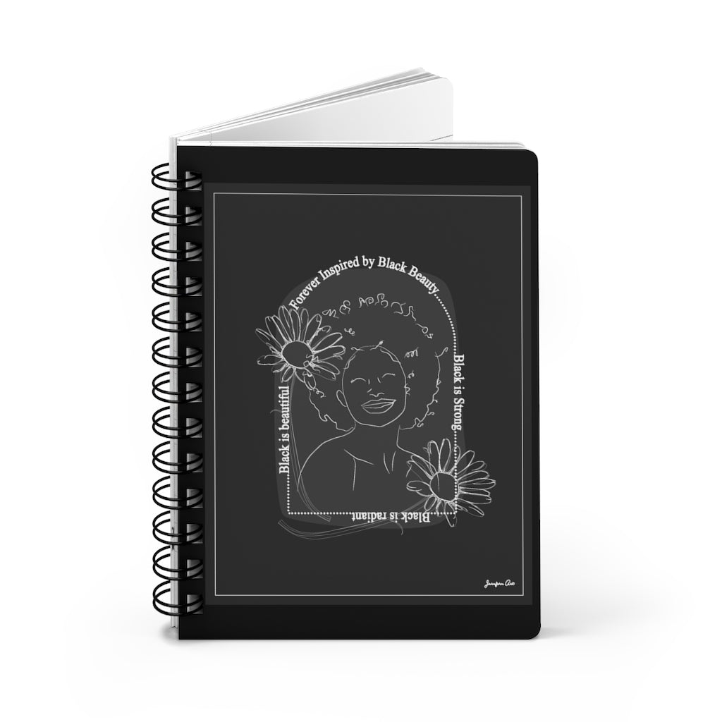 A monochrome spiral journal with a line drawing on the cover of a Black woman with an afro surrounded by flowers and text that reads "Forever Inspired by Black Beauty"