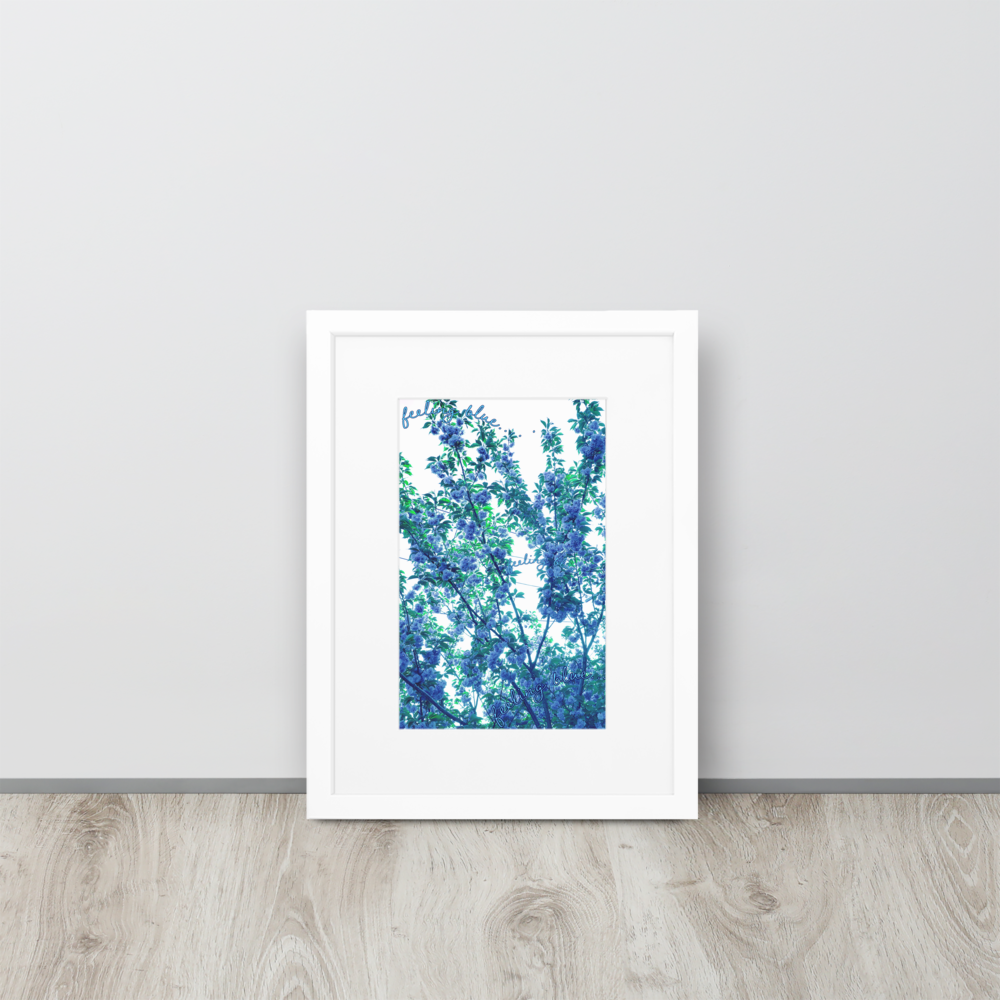An abstract blue floral photo inside of a white frame, standing up on a wood floor against a white wall