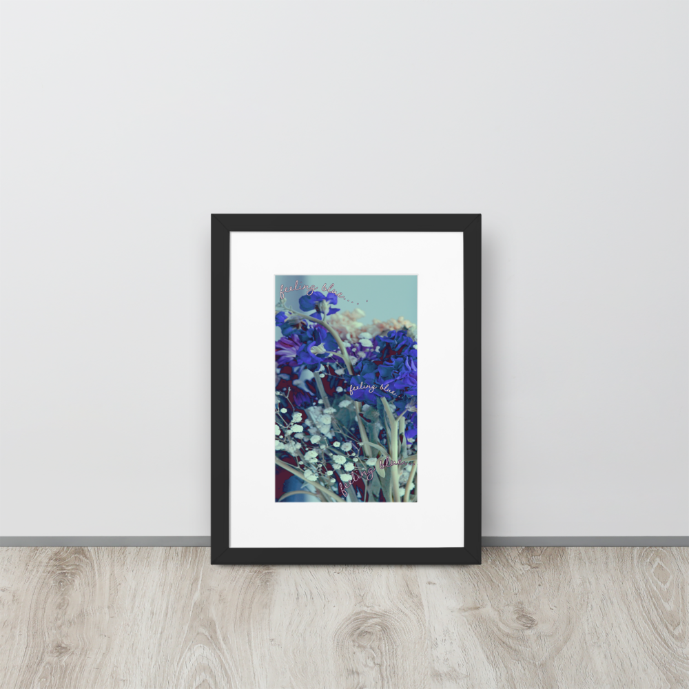 A close-up blue and purple flower bouquet photo inside of a black frame with a white mat boarder, standing up on a wood floor