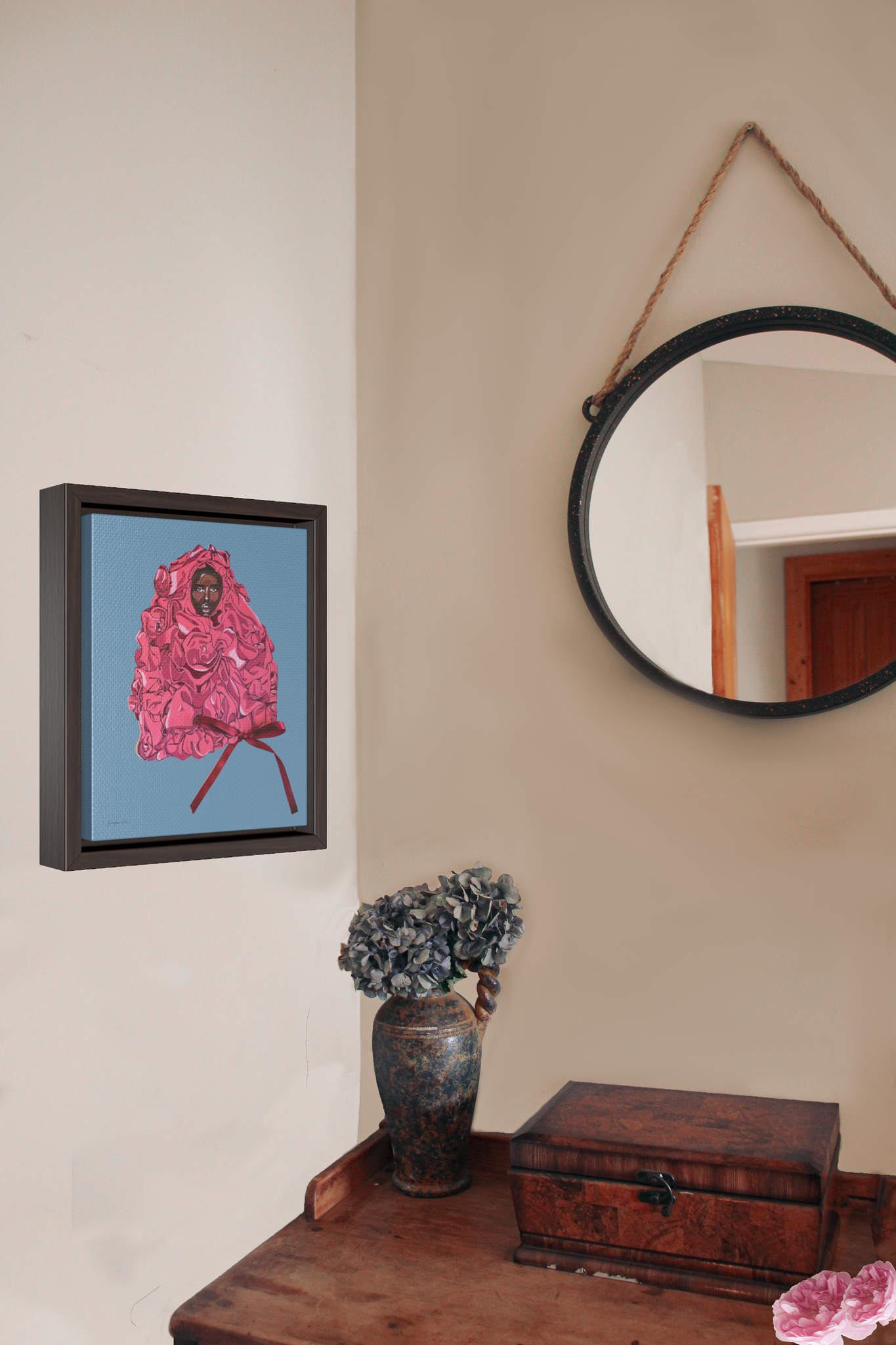 A framed gallery wrap canvas, with an illustration of model Adut Akech wearing a pink Valentino gown with a bow, with a light blue background, hanging on a wall next to a desk with a vase of flowers and a jewelry box