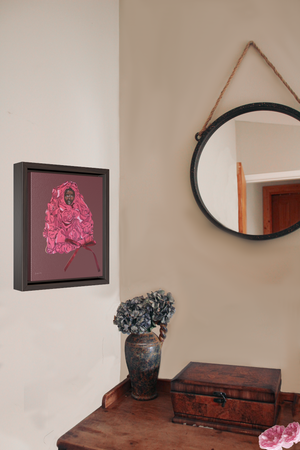 A framed gallery wrap canvas, with an illustration of model Adut Akech wearing a pink Valentino gown with a bow, with a dark pink background, hanging on a wall next to a desk with a vase of flowers and a jewelry box
