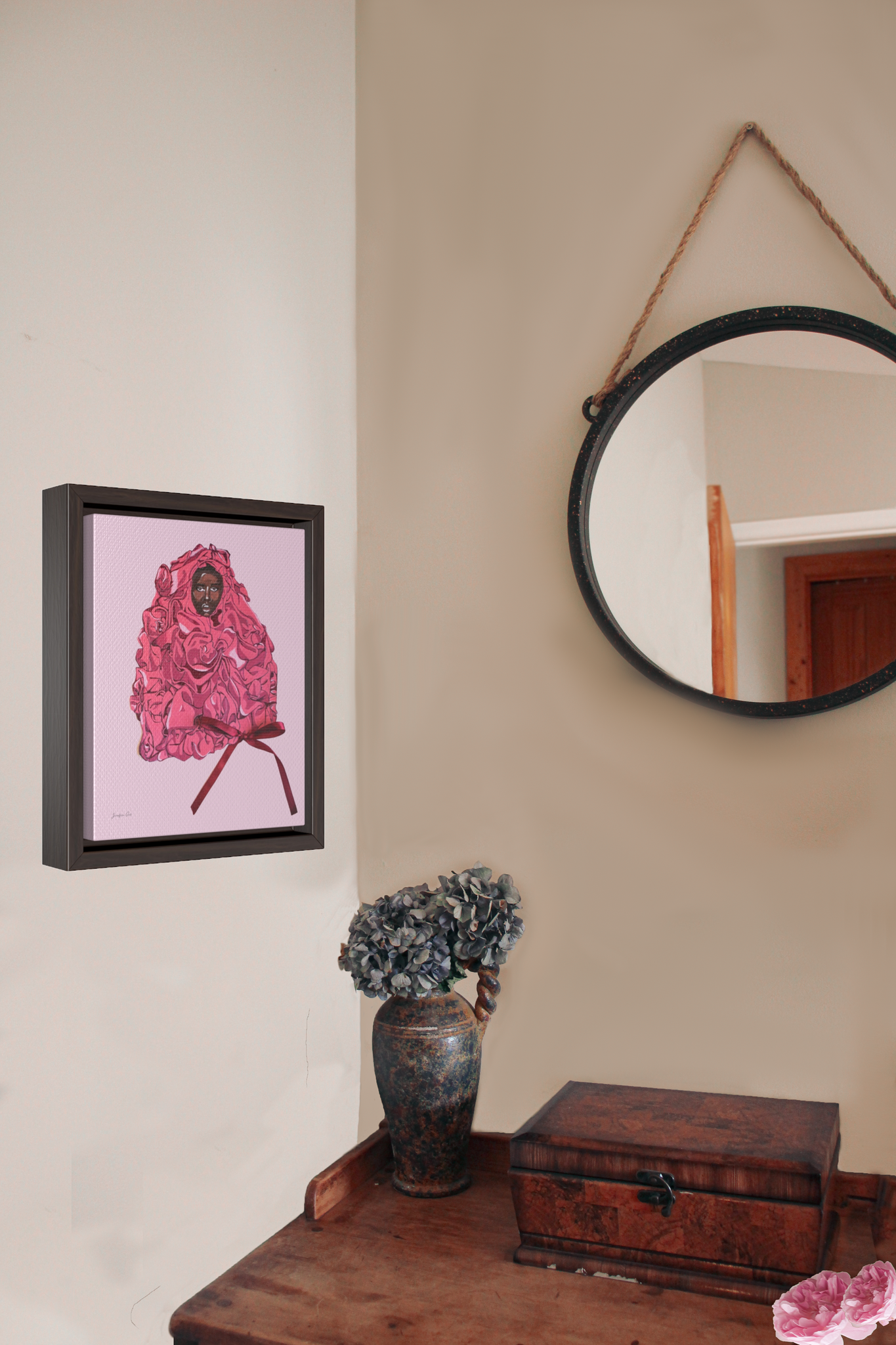 A framed gallery wrap canvas, with an illustration of model Adut Akech wearing a pink Valentino gown with a bow, with a light pink background, hanging on a wall next to a desk with a vase of flowers and a jewelry box