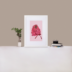 A white framed print with white board matting, with an illustration of Black supermodel Adut Akech wearing a pink Valentino gown with a bow on it, with a light pink background, standing up on a table next to a green plant and a stack of books