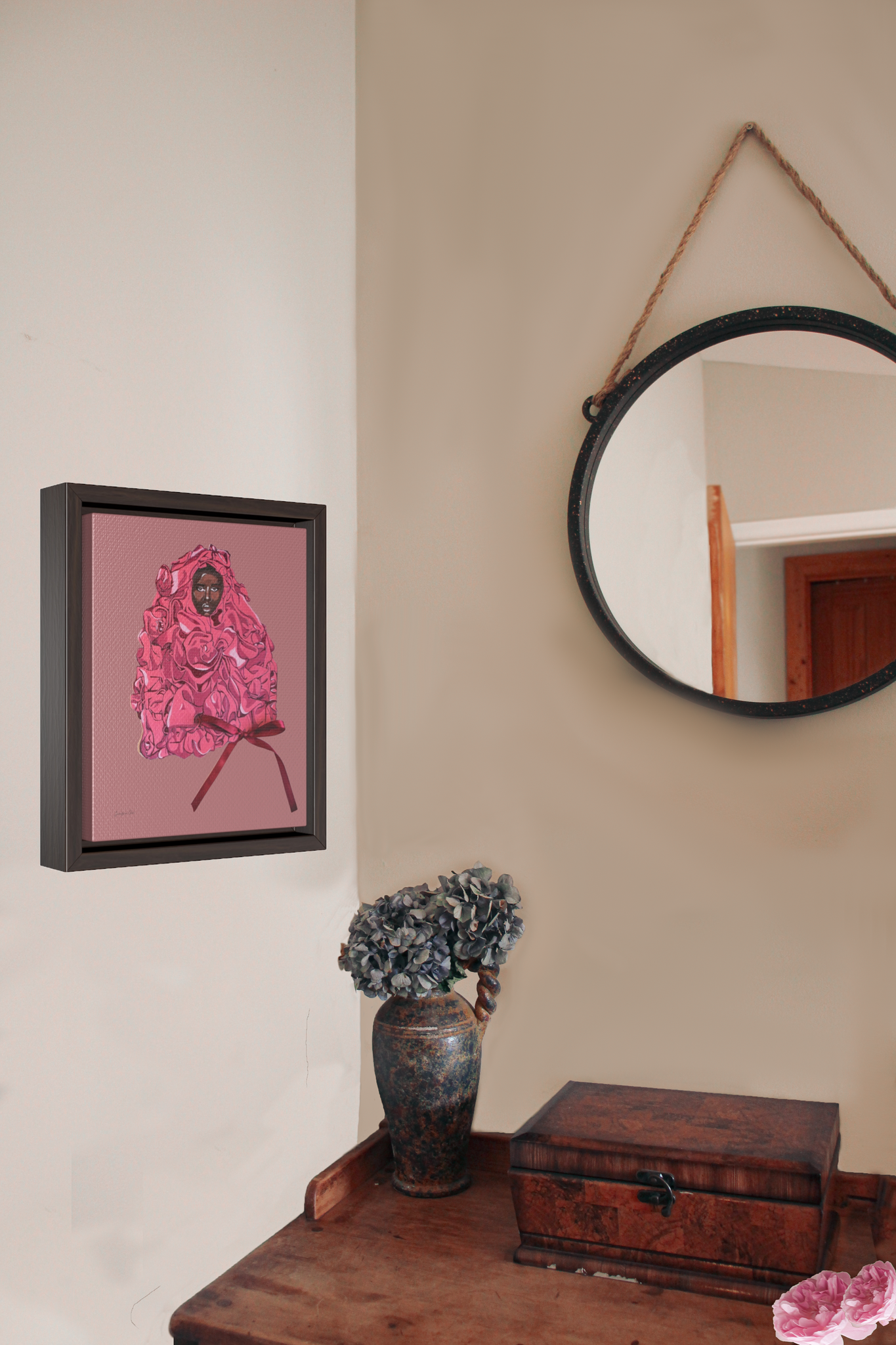 A framed gallery wrap canvas, with an illustration of model Adut Akech wearing a pink Valentino gown with a bow, with a pink background, hanging on a wall next to a desk with a vase of flowers and a jewelry box