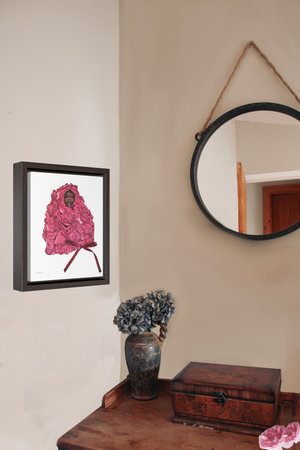 A framed gallery wrap canvas, with an illustration of model Adut Akech wearing a pink Valentino gown with a bow, with a white background, hanging on a wall next to a desk with a vase of flowers and a jewelry box