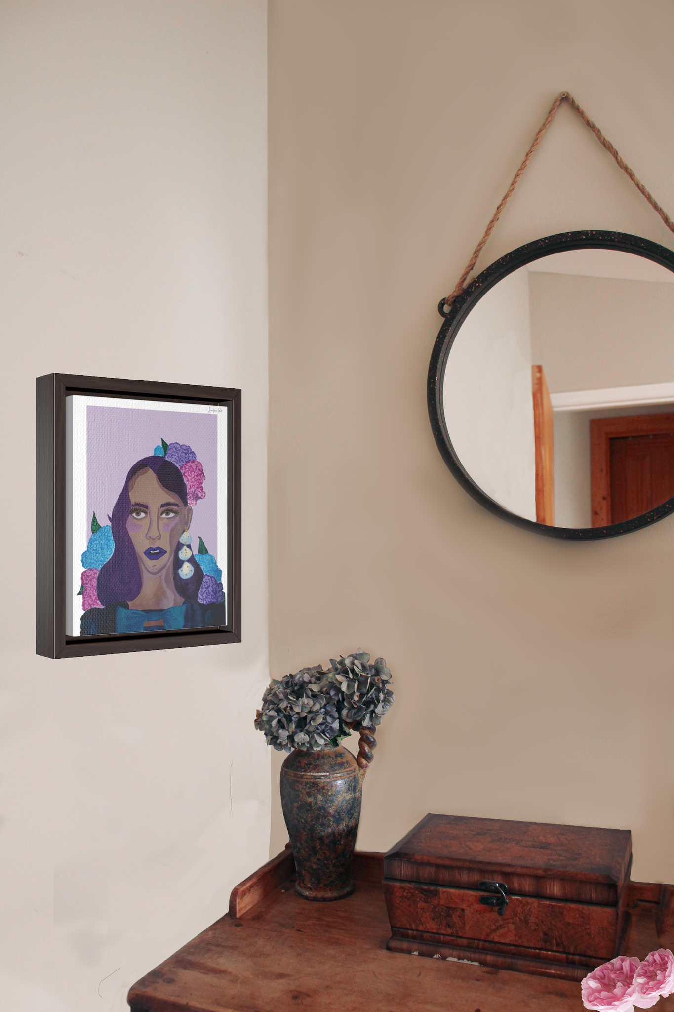 A framed canvas illustration of a Black woman painted in purple hues and wearing a blue dress with a blow in front and hydrangea flowers in her hair, hanging on a wall next to a circle mirror and a wood desk with a flower vase and jewelry box