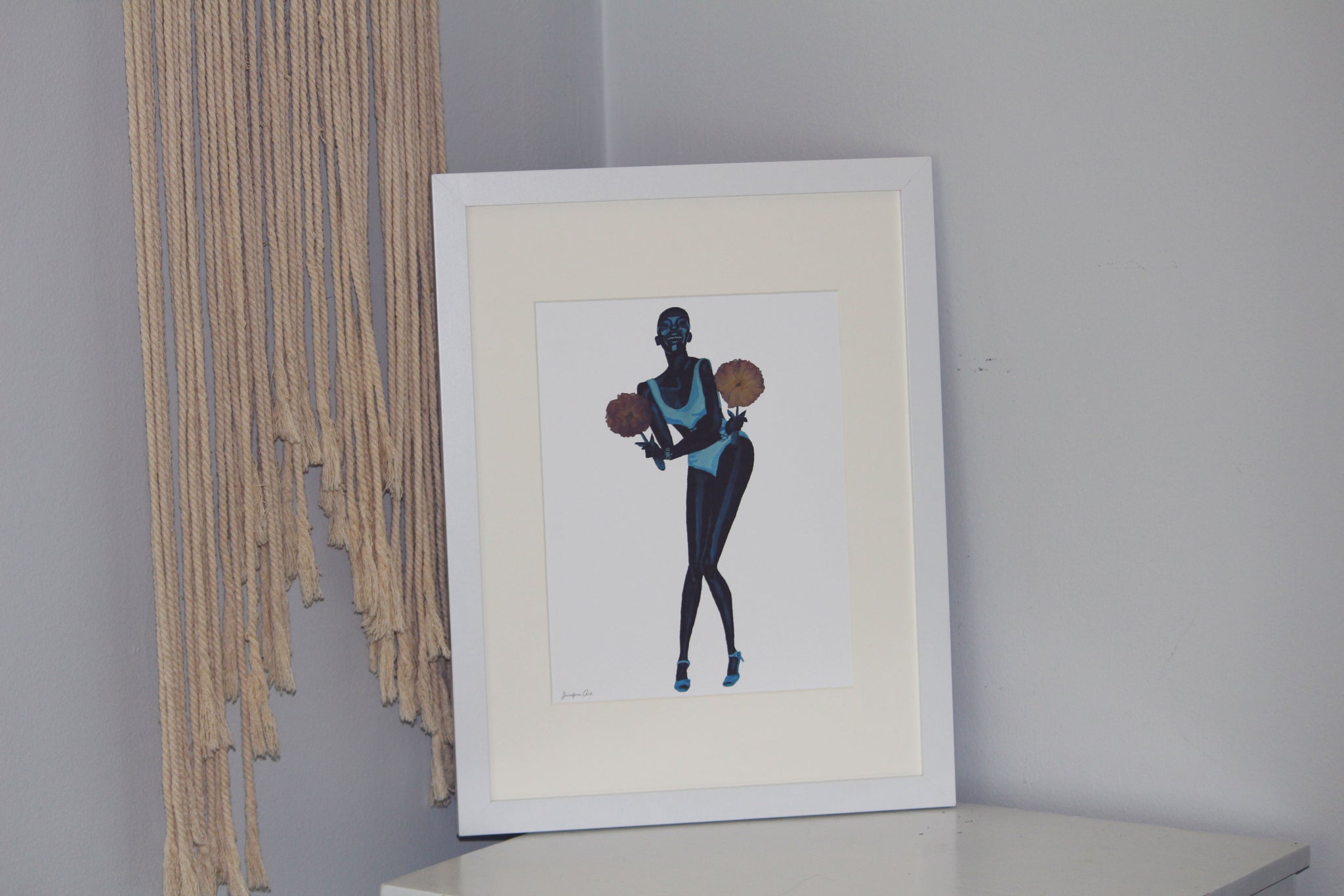8.5 by 11 inch Black fashion art print of a painting of Adut Akech wearing a Chanel swimsuit and holding pressed flowers with a white background in a white frame with matting standing up on a white table