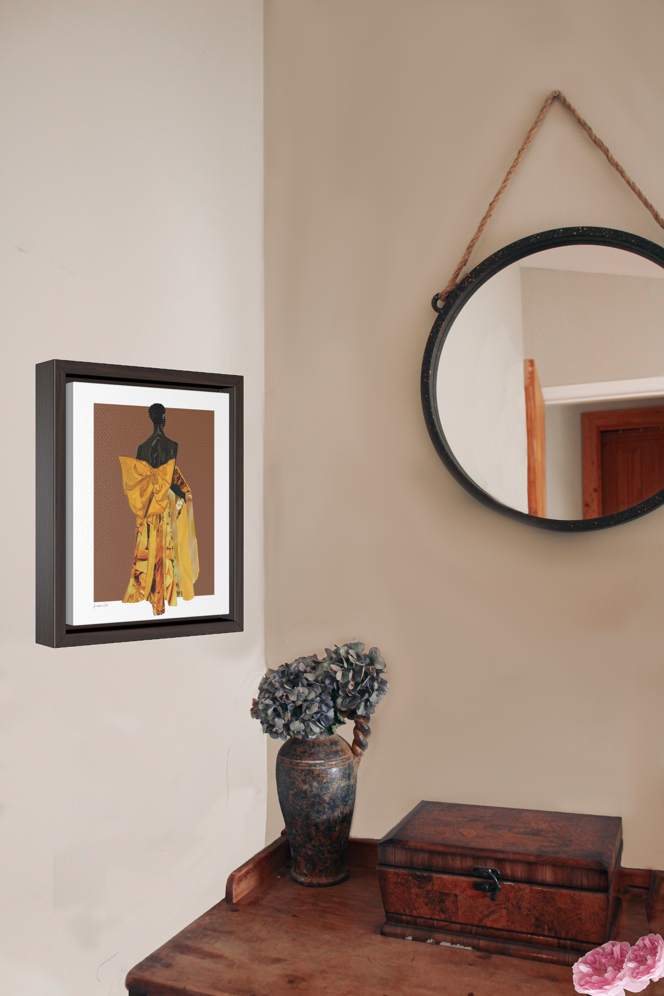 A framed canvas featuring a fashion illustration of Black model Akiima Ajak wearing a yellow Valentino gown with a large bow on the back, and a brown background, hanging on a wall above a wood desk with a vase of flowers