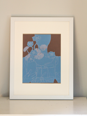 A monochrome blue graphic illustration of a woman in a top with bows holding a vase of flowers, with a brown background, inside of a white frame standing up on a white table in front of a white wall