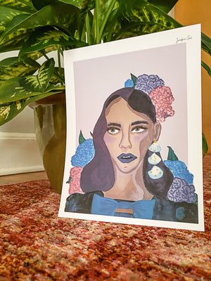 An illustration print of a portrait of a Black woman, painted in purple hues, wearing a blue velvet dress with a bow in the front and blue and pink hydrangeas in her hair, leaning up against a large potted leafy plant