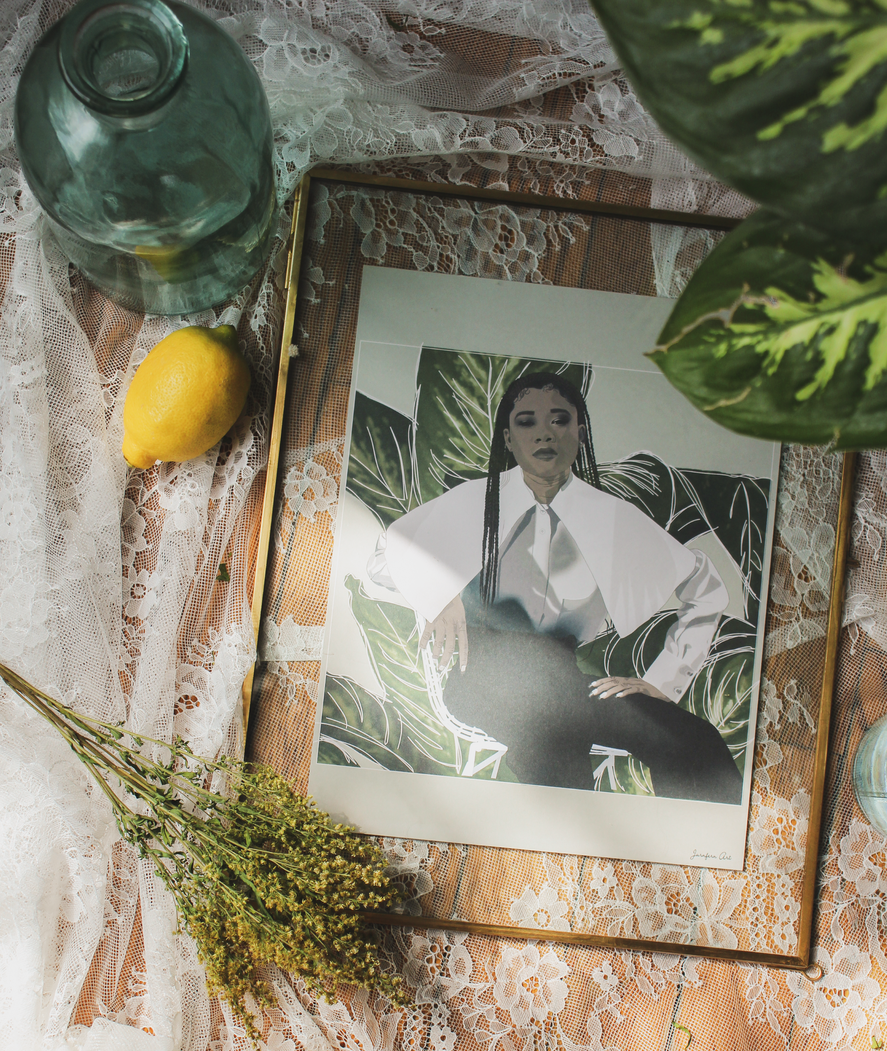 An illustration print with a beige background and a digital illustration of actress Storm Reid posing in a chair and wearing a white Nina Ricci blouse and black trousers with leaves behind her, inside of a transparent frame that is lying on a lace tablecloth next to flowers, a vase, and a lemon